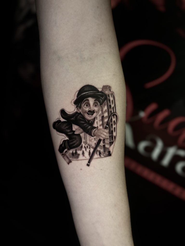 Sude Kara'nın Charlie Chaplin karakteri ve şehir manzaralı siyah gri dövmesi
